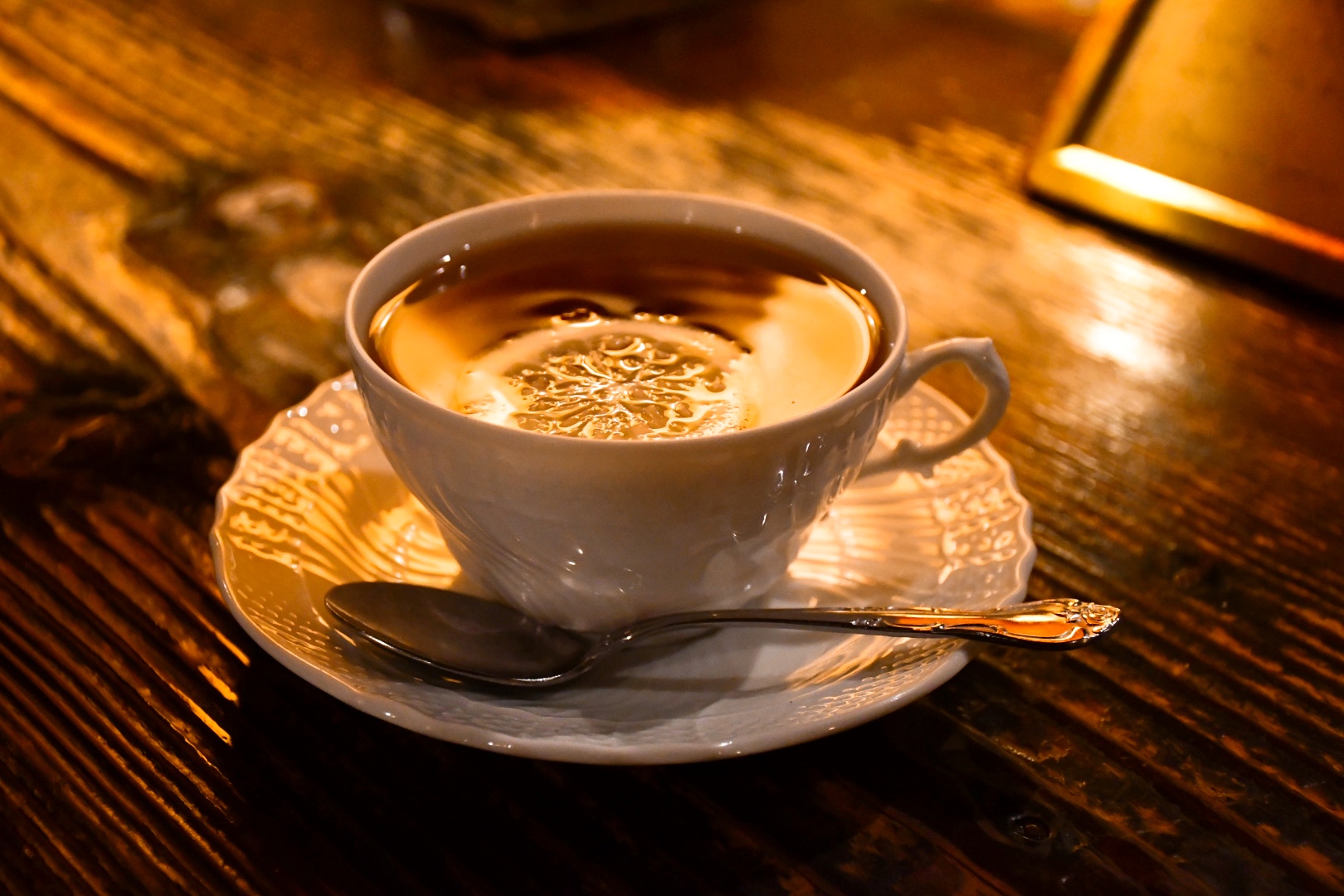 木製カウンターの上に白い陶器カップのコーヒーと銅製スタンド、奥の棚に整然と並ぶカップ類