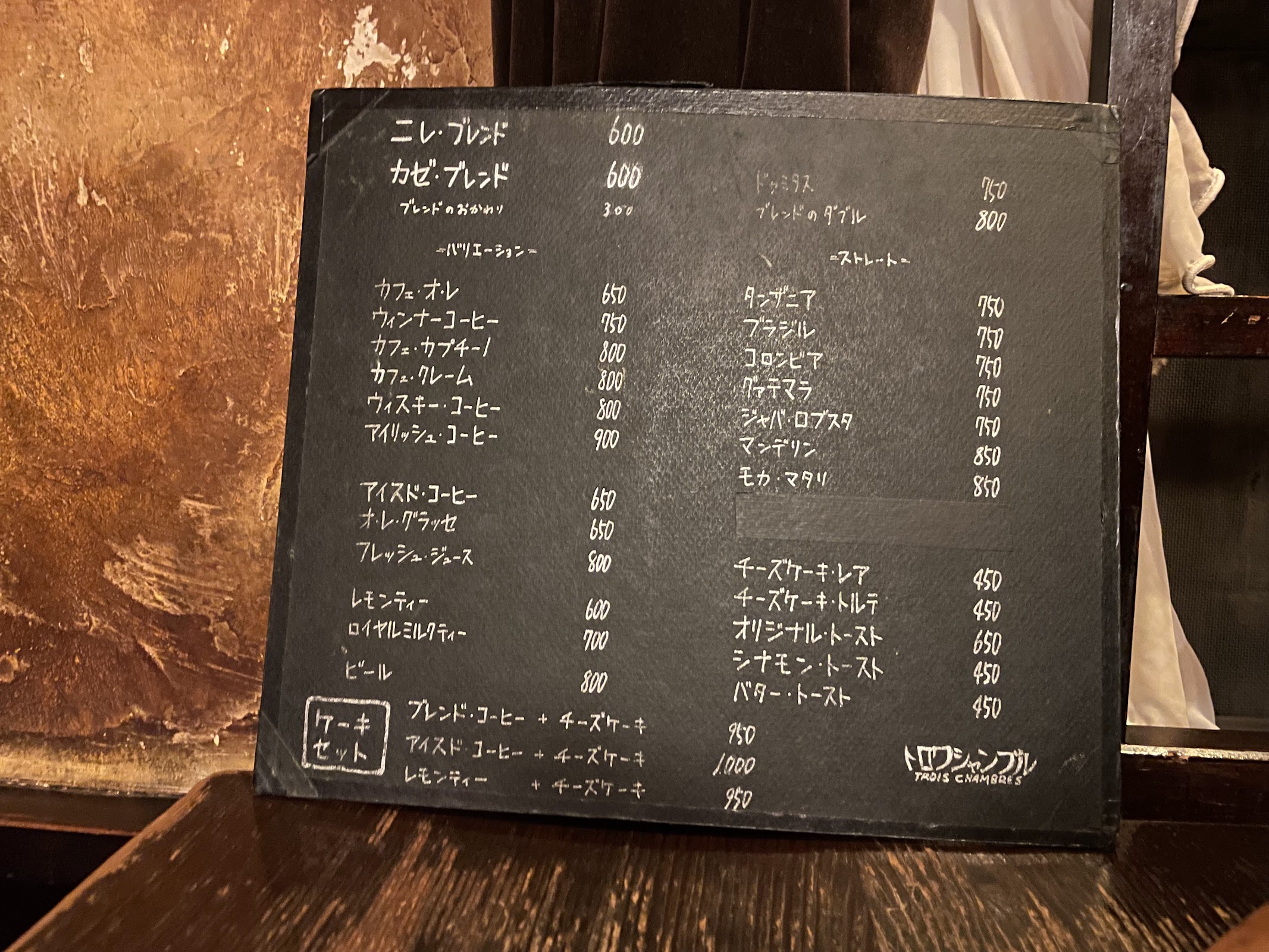 黒板に白チョークで書かれたトロワ・シャンブルのメニュー表。ニレ・ブレンド600円、カゼ・ブレンド600円など手書きの価格一覧